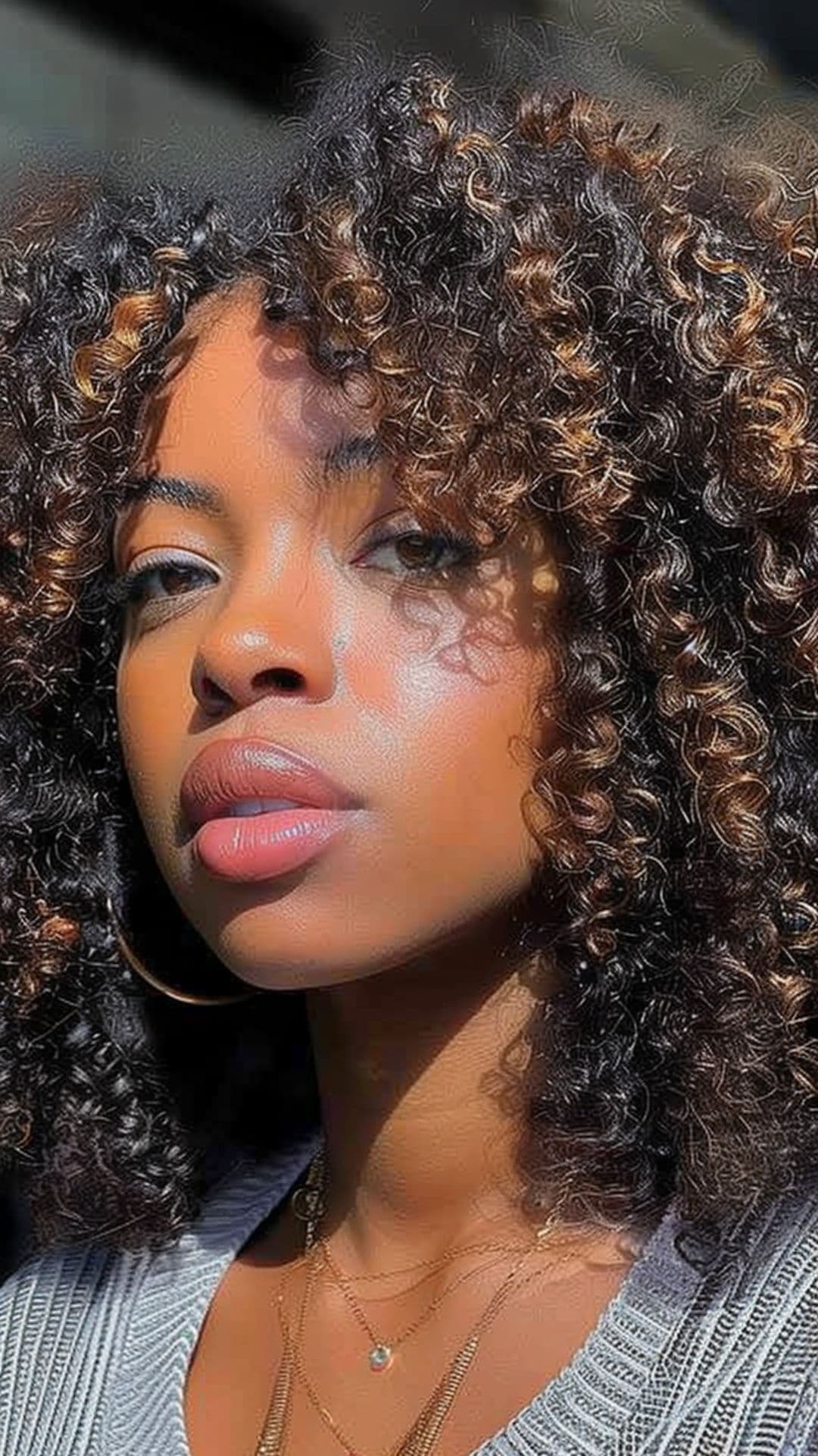 A black woman modelling a bronze highlights on afro hair.